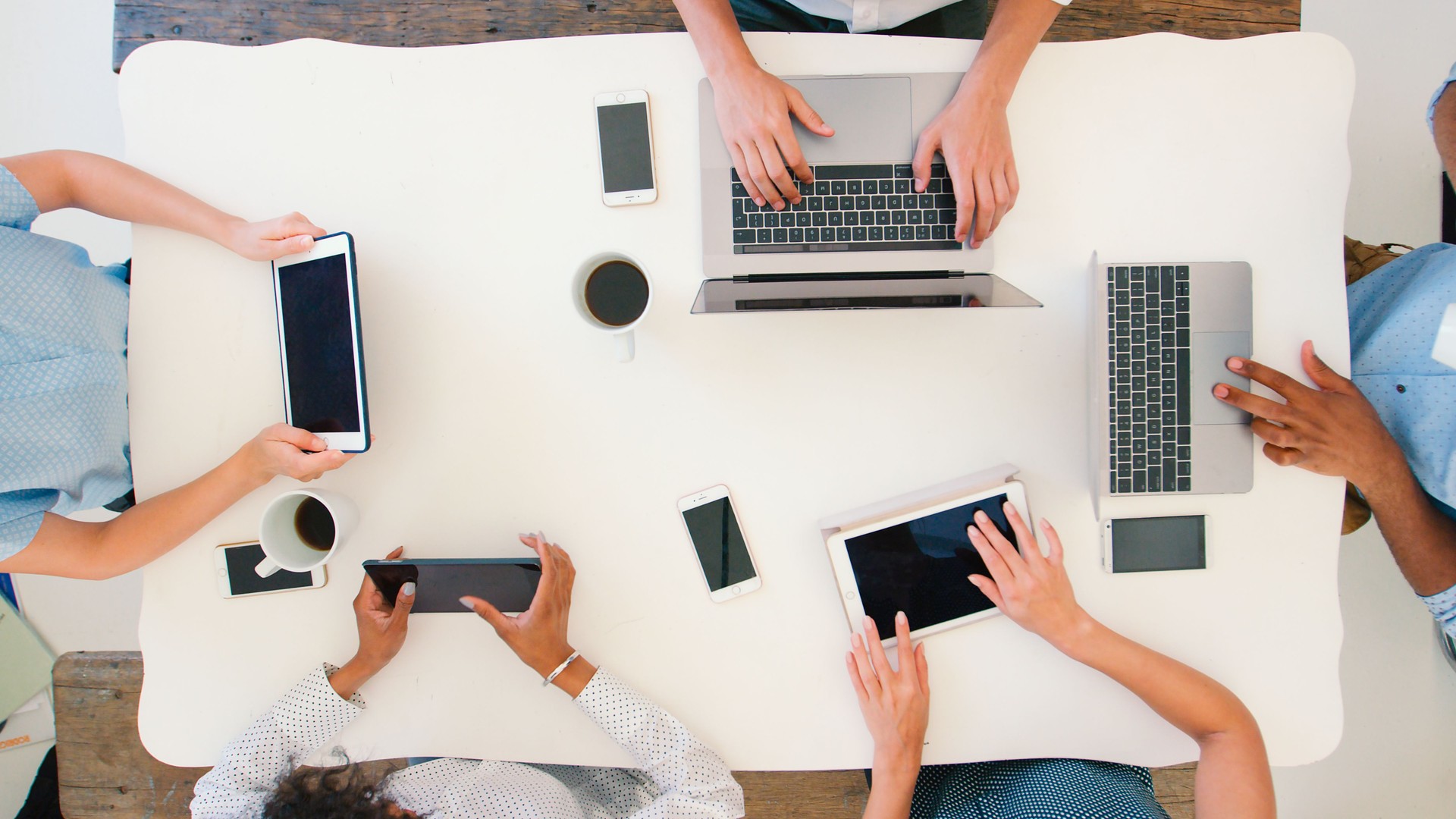 Overhead Shot Of Business Team Meeting Around Table Working On Digital Devices